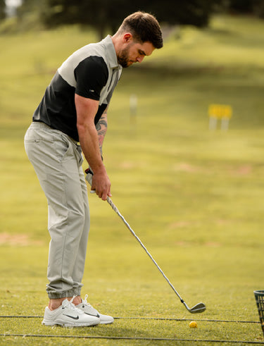 Man wearing golf trousers in grey and preparing to putt a golf ball on a green golf course
